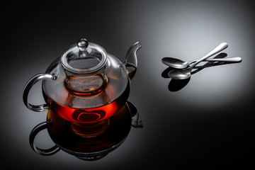 glass teapot with hot tea and spoons on table, close view  