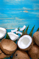 Wall Mural - Whole coconut, shell, green palm leaves on a blue wooden background. Copy space. Top view, flat lay. Tropical background.