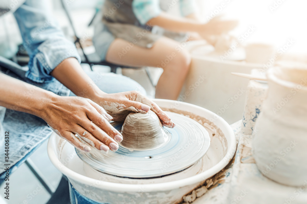 Close-up of female hands sculpting clay on a Potter's wheel. Concept of hobby and cretivity at home and in the Studio workshop - obrazy, fototapety, plakaty 
