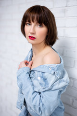 Wall Mural - portrait of young sexy woman with red lips in jeans shirt posing over white brick wall