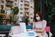 © Dragica - Attractive young caucasian woman with mask, gloves working on laptop in cafe