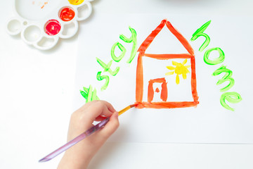 Wall Mural - Top view child is drawing red house by watercolors with words Stay Home on white sheet of paper. Stay Home concept.