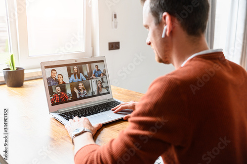 A guy is using app for video conference, video call on laptop. He talks online with a several friends together. Side view
