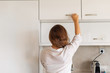 © flowertiare - Back view of woman putting or taking clean plate on the shelf in kitchen cupboard. Housework Concept.