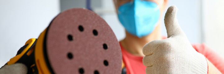 Masked carpenter holds tool and shows gesture ok