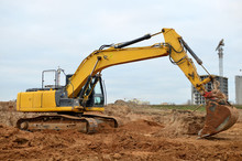 Excavator With A Large Iron Bucket On A Construction Site During Road Works. Backhoe Dig The Ground For The Foundation, Laying Storm Sewer Pipes. Installation Of Water Main Systems.