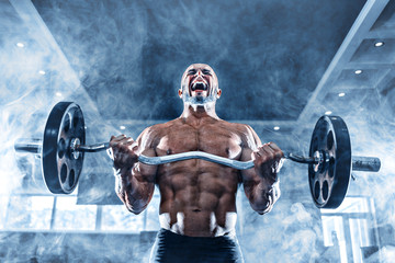 Muscular man working out in gym doing exercises with dumbbells at biceps, strong male naked torso abs in smoke.