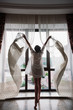 © Nina_Arnis - Woman silhouette opening curtains and looking out of window in the room at morning. panoramic windows with view in the garden. full height young girl. Young girl is ready for new plans and challenges