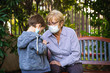 © progat - Grandmother and little kid playing with a smartphone in the backyard while wearing protective masks due to coronavirus outbreak