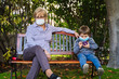 © progat - Grandmother and little kid playing with a smartphone in the backyard while wearing protective masks due to coronavirus outbreak
