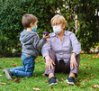 © progat - Grandmother and little kid playing with a smartphone in the backyard while wearing protective masks due to coronavirus outbreak