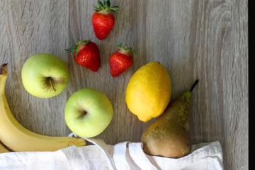 Canvas tote bag with bananas, apples, pear, lemon and strawberries. Top view.