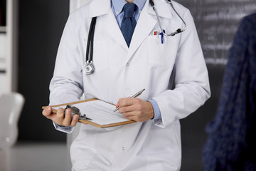 Unknown red-bearded doctor and patient woman discussing current health examination while sitting in sunny clinic, close-up. Medicine concept