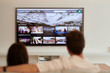 © guille Faingold/Stocksy - TV on wall and couple against on sofa.