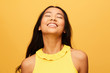 © leandro crespi/Stocksy - Happy asian Woman portrait with eyes closed laughing isolated over yellow