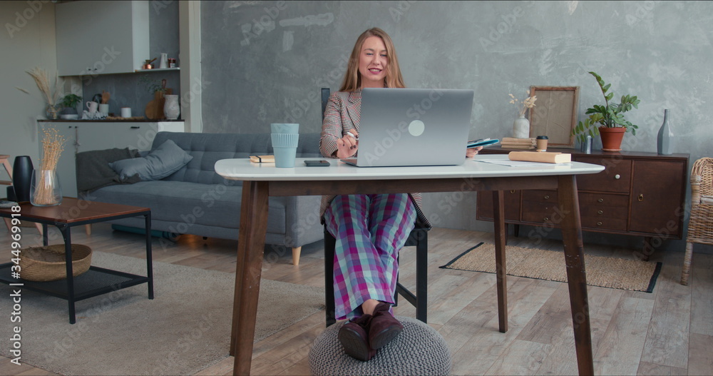 Comfortable work from home on lockdown. Young cheerful business woman in pajamas pants using laptop video conference app - obrazy, fototapety, plakaty 