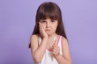 © sementsova321 - Studio shot of upset little girl posing isolated over lilac studio background, keeping palm on cheek, looks sad, has toothache, child's first teeth fall, kid holds tooth brush in hand, looks at camera