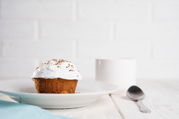 Cupcakes with whipped cream and chocolate chips on a white plate and a Cup of coffee in the background, on a white wooden table. Image for the menu or catalog of confectionery products.