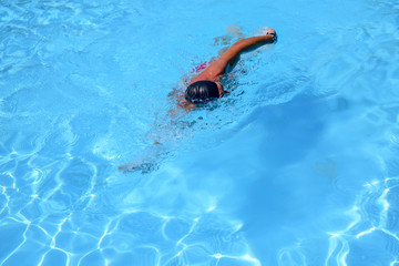 Caucasian man swims in freestyle (crawl) at the outdoor swimming pool on a sunny summer day