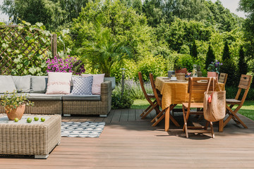 Dining table covered with orange tablecloth standing on wooden terrace in green garden