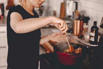 Lady cooks dinner for family. Dutch oven on stove top. Lifestyle kitchen. Stewed potatoes. Seasoning with salt, stiring meal. Hot meal. Cook process. Dinner preparation. Kitchen towel. Red dutch oven