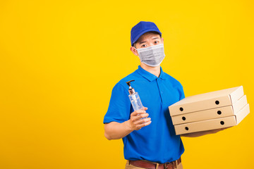 Wall Mural - Asian young handsome delivery man wearing face mask protective germ virus holding alcohol sanitizing gel and boxes on hand, studio shot isolated on yellow background, outbreak coronavirus COVID-19