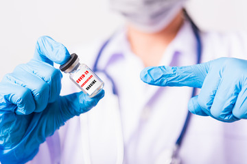 Asian female woman doctor or nurse in uniform, gloves wearing face mask protective in laboratory pointing vial corona vaccine bottle on hand and bottle have 