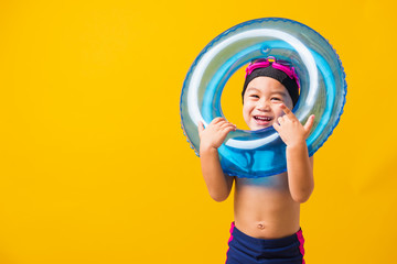 Summer vacation concept, Portrait Asian happy cute little child boy wear goggles and swimsuit hold blue inflatable ring, Kid having fun on summer vacation, studio shot isolated yellow background