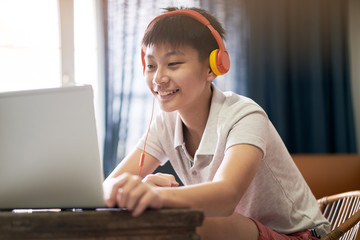 Asian teenage boy studying at home during pandemic wearing headset and smiling