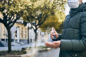 Cropped close-up snapshot of hands of woman, in the street, wiping her hands with hand-washing spray as preventive hygiene measure against Covid-19 infection. Keep social distance, spring 2020