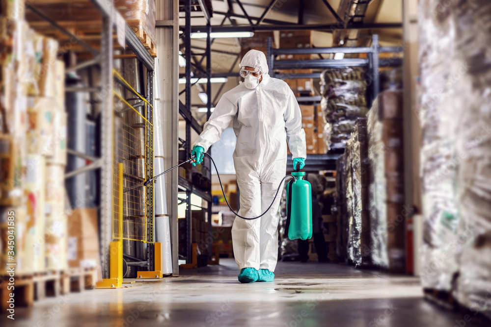 Man in protective suit and mask disinfecting warehouse full of food products from corona virus / covid-19. - obrazy, fototapety, plakaty 