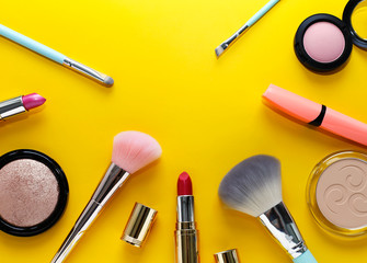 Wall Mural - Beautiful makeup: pink lipstick, blush, powder, cosmetic brushes on a bright yellow background
