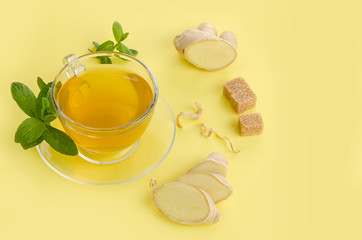 Wall Mural - Ginger tea with lemon in glass Cup with brown organic sugar and mint on yellow paper background