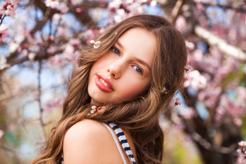 young girl posing near blossom cherry tree with pink flowers