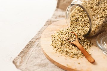 Cannabis kernels in a glass jar on a white table with a wooden spoon