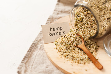 Cannabis kernels in a glass jar on a white table with a wooden spoon