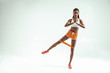 Fitness everyday. Full length of young and slim african woman in sports clothing exercising with a resistance band and looking at camera while standing in studio against grey background