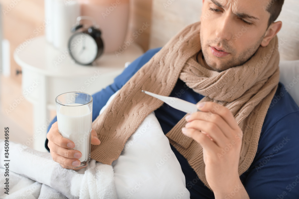 Young man ill with flu drinking milk in bed