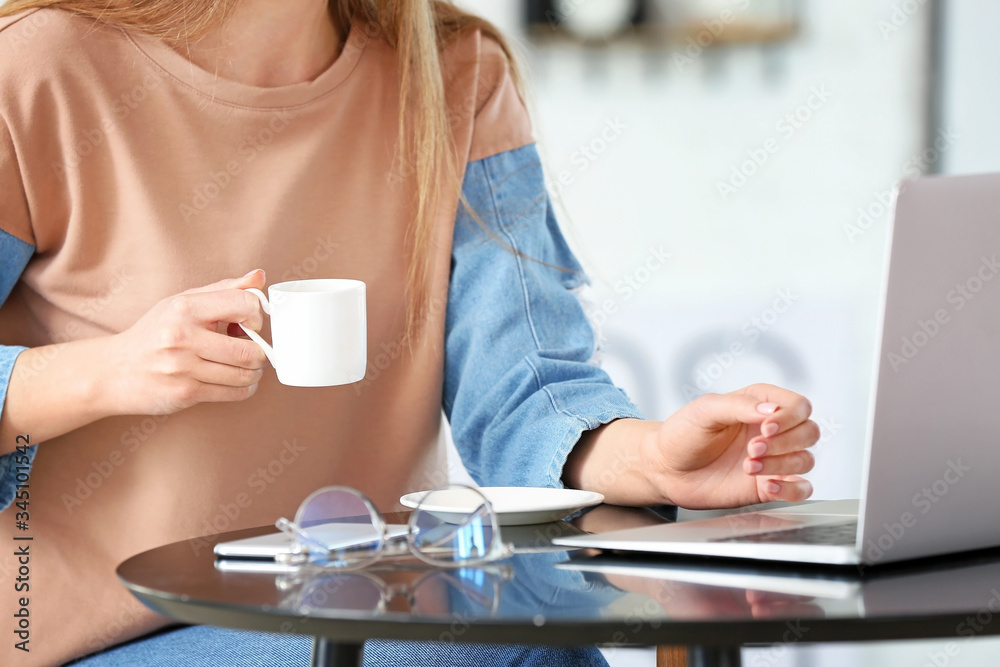Young woman drinking coffee while working on laptop in cafe