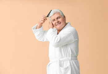 Wall Mural - Mature man in bathrobe combing his hair on color background