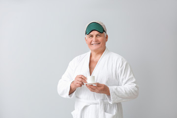 Wall Mural - Happy mature man in bathrobe, with sleep mask and cup of coffee on grey background