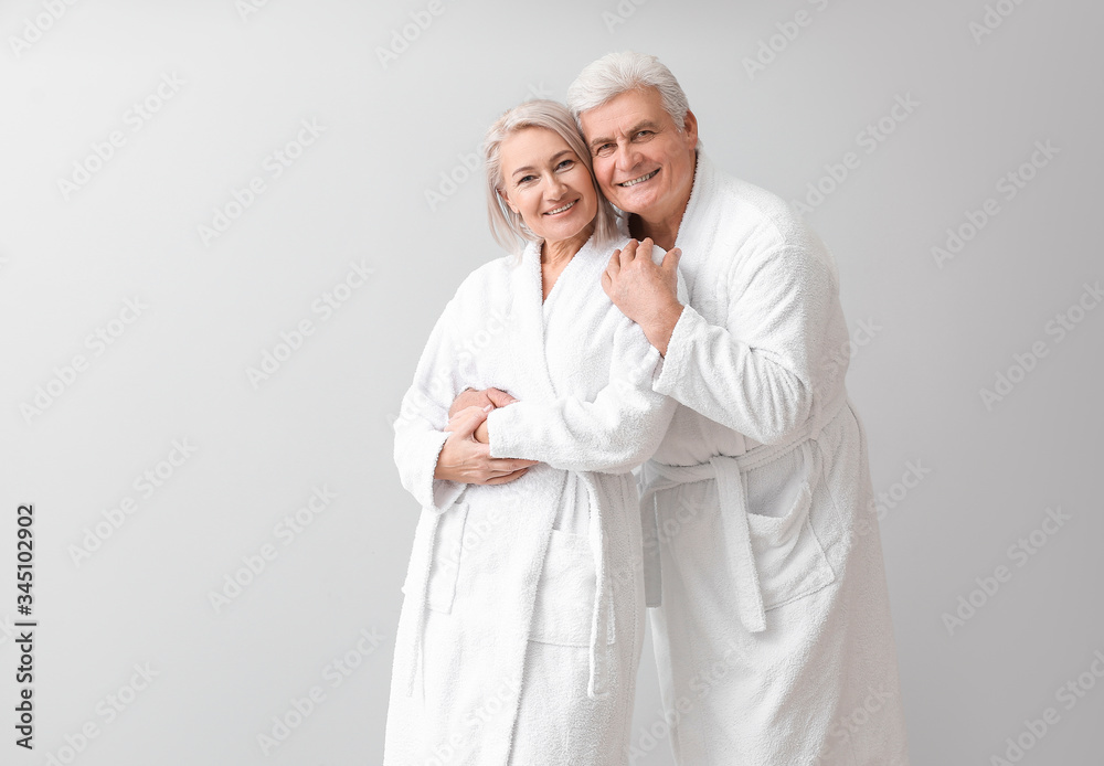 Mature couple in bathrobes on grey background