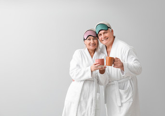 Poster - Mature couple in bathrobes and with sleep masks drinking tea on grey background