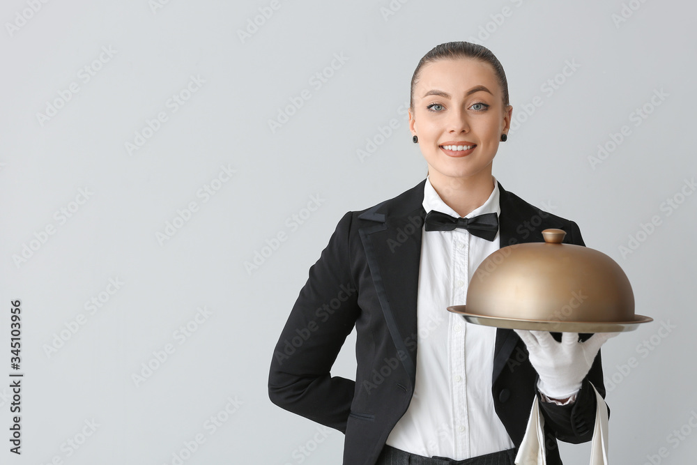 Female waiter with tray and cloche on grey background
