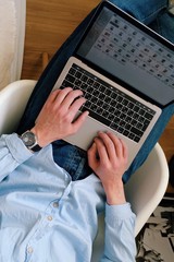 Vertical shot of a male wearing a blue shirt and jeans while working on a laptop