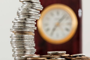 Sticker - Selective focus shot of coins placed on each other and a clock in the background- 