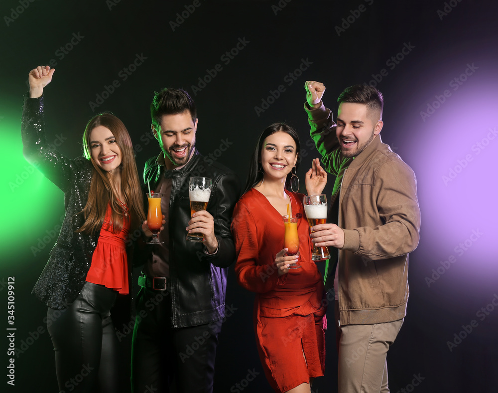 Happy young people with alcoholic drinks on dark background