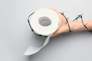 Female hand with toilet paper and barbed wire on light background. Hemorrhoids concept