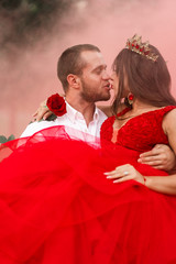 Wall Mural - Beautiful romantic couple Attractive young woman in red dress and crown with handsome man in white shirt are dancing on pink smoke.Baby gender Happy Saint Valentine's Day.Pregnant and wedding concept.