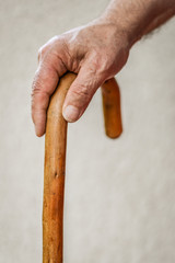 Closeup of senior man's hand on wooden walking stick. Selective focus on fingers.